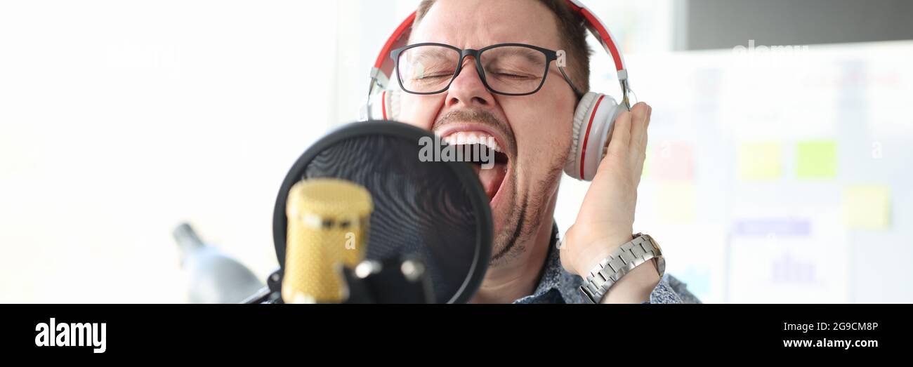 Jeune homme dans un casque chantant dans un micro. Concept de chant émotionnel Banque D'Images