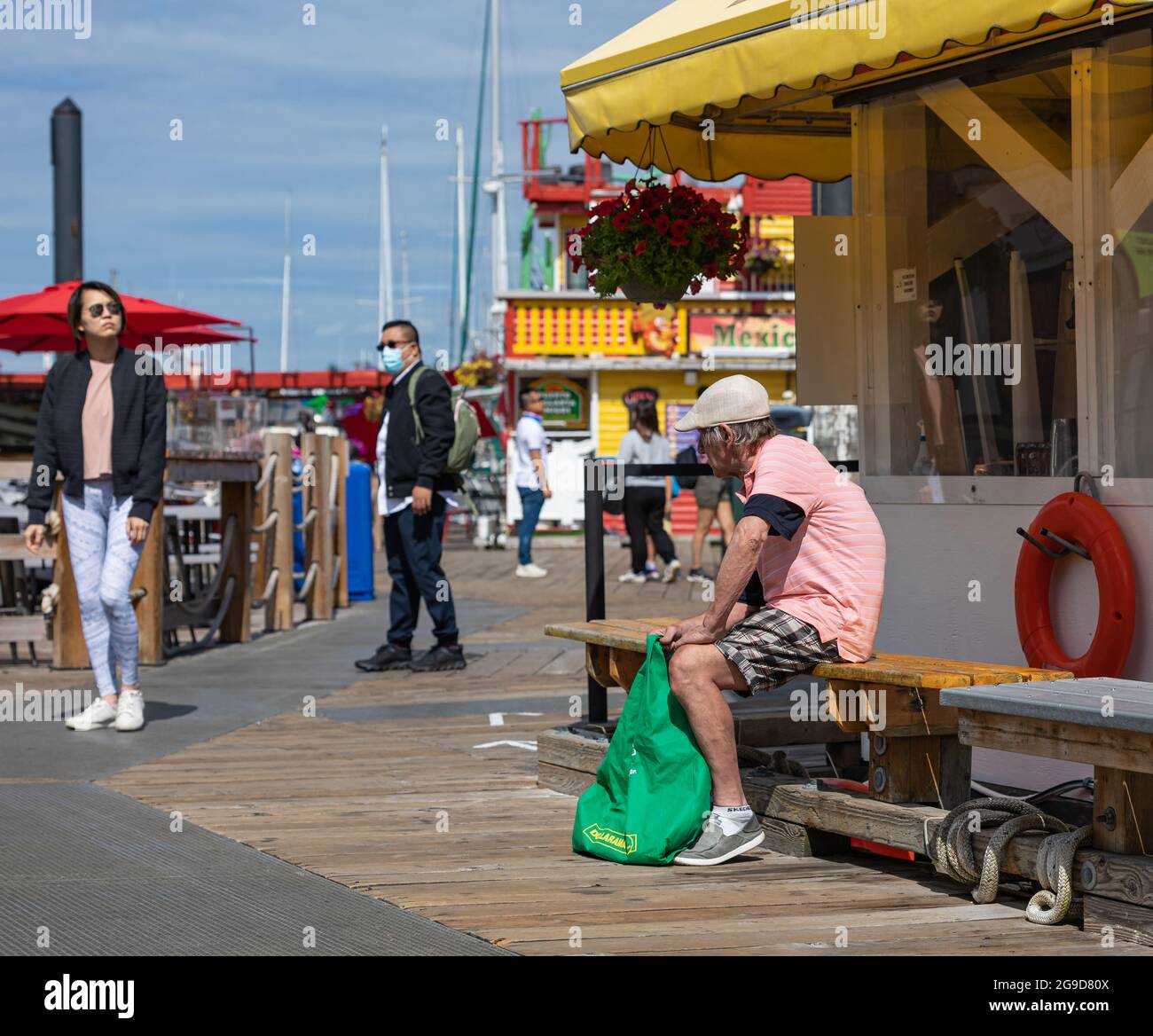 Vue latérale d'un triste pauvre assis sur le banc de bois par une journée ensoleillée à Fisherman Wharf Victoria, C.-B., Canada-juillet 23,2021. Vue sur la rue, photo de voyage Banque D'Images