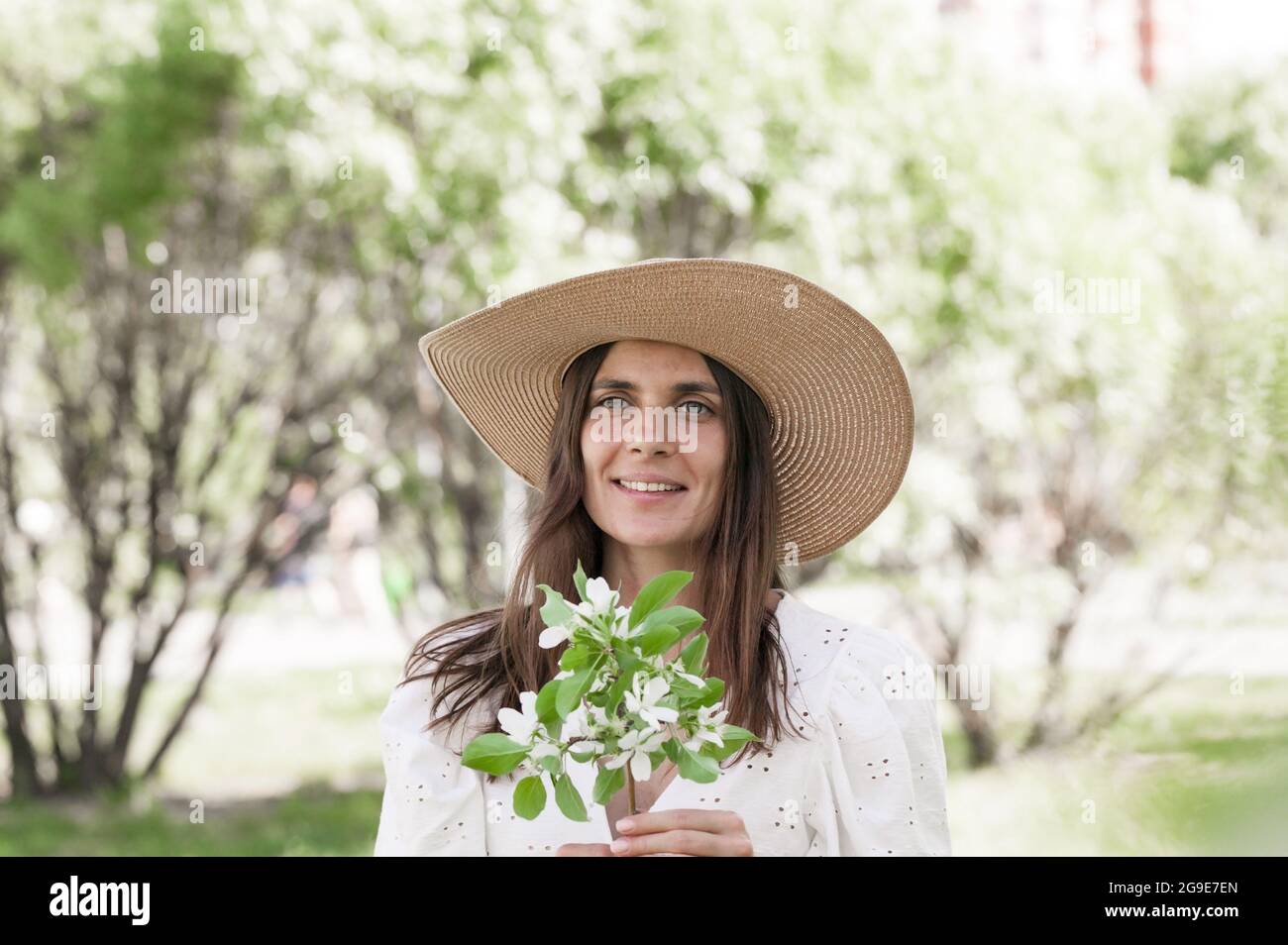 Jolie et heureuse femme pose dans un chapeau de paille sur le parc de printemps. Jeune femme souriante sur le fond des pommiers en fleurs. Heure d'été. Attrayant Banque D'Images