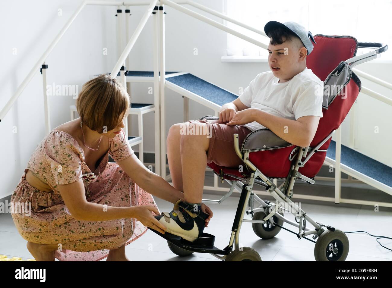 Mère aidant un garçon handicapé de 17 ans en fauteuil roulant avec paralysie cérébrale à mettre des chaussures, avant d'aller pour une promenade. Femme aide la personne avec spécial Banque D'Images