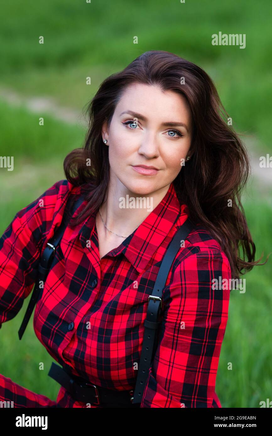 Portrait d'une jolie dame tendance en robe-chemise à carreaux rouge posé  sur toile de fond de la nature. Jeune fille à la mode dans le parc le jour  de l'été Photo Stock -