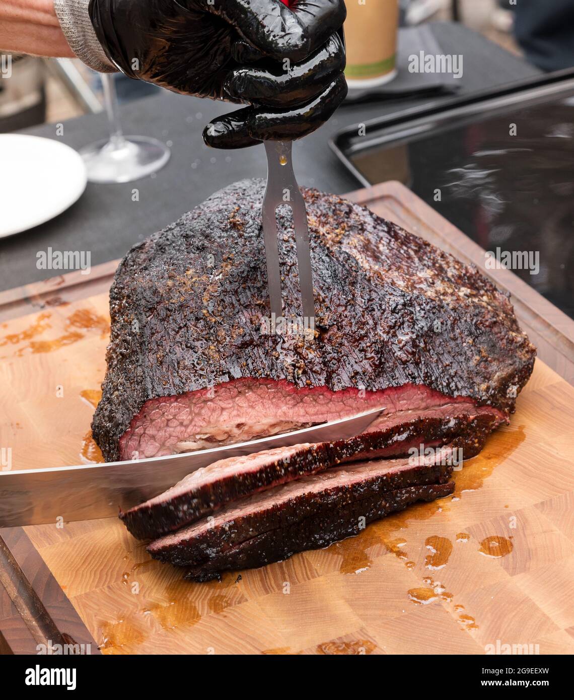 Chef sculptant une portion de succulente poitrine de bœuf épicée marinée sur une planche à découper en bois en gros plan sur la lame du couteau Banque D'Images
