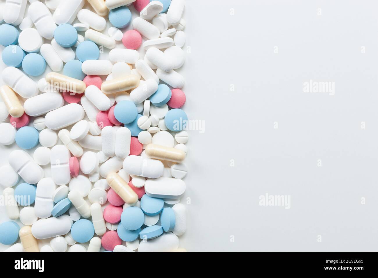 Pile de pilules et capsules de couleur bleue, blanche, rose et jaune sur le côté gauche du fond blanc avec espace de copie sur la droite Banque D'Images