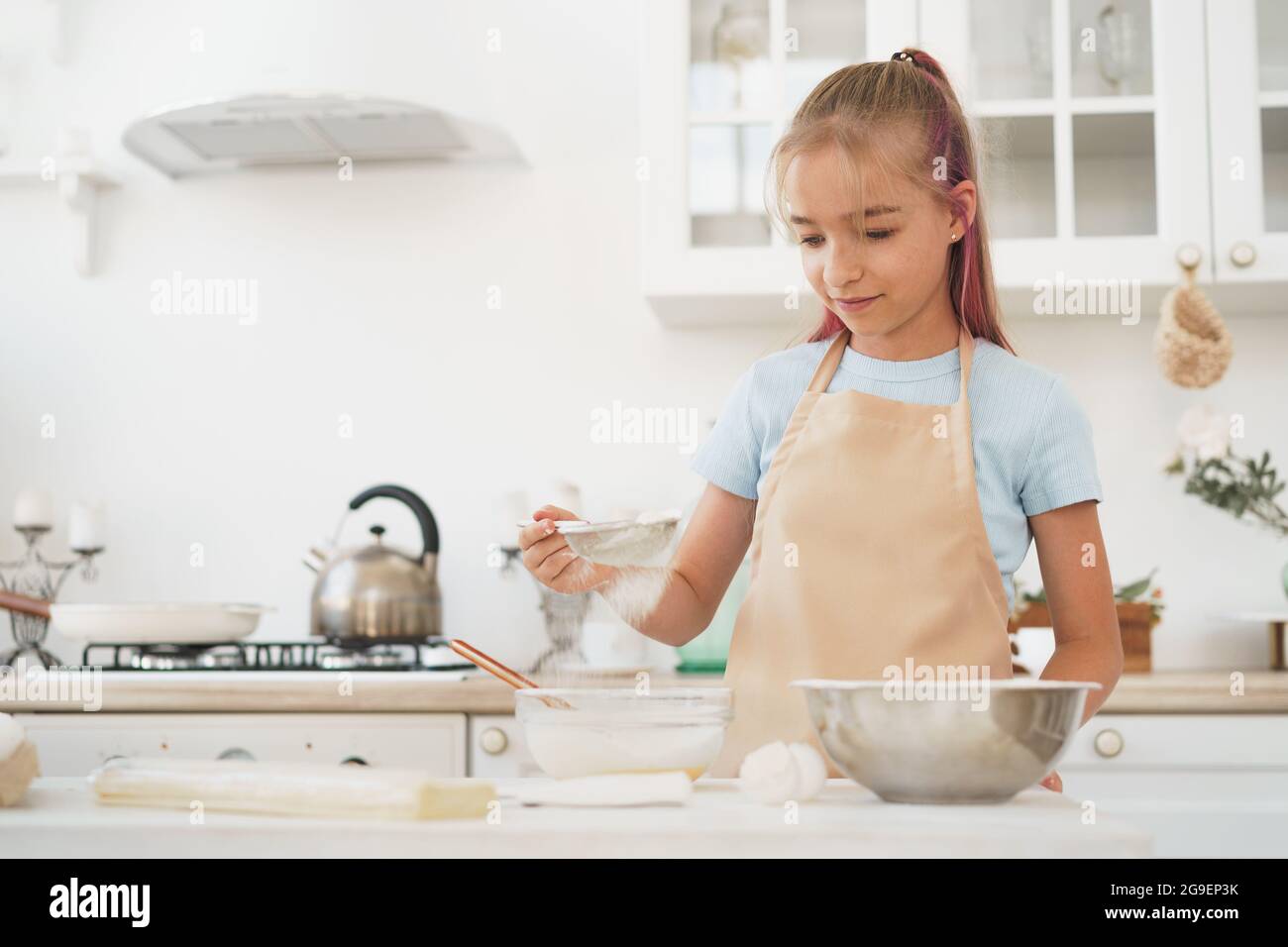 Portrait d'une petite fille blonde de l'adolescence portant un tablier dans la cuisine Banque D'Images