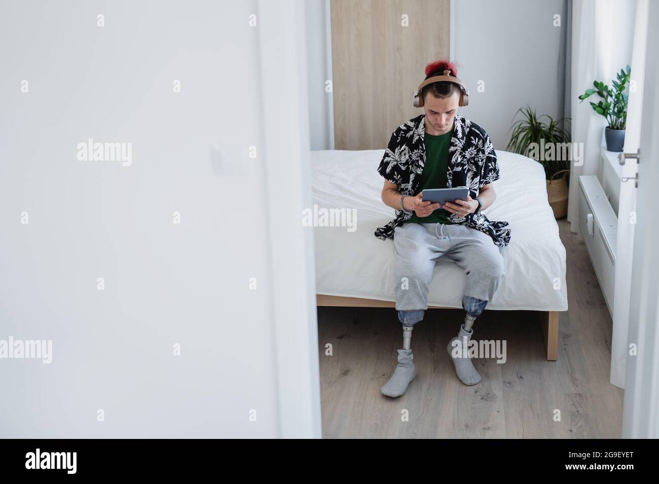 Portrait d'un jeune homme handicapé utilisant une tablette sur le lit à l'intérieur à la maison, concept prothétique de jambe. Banque D'Images