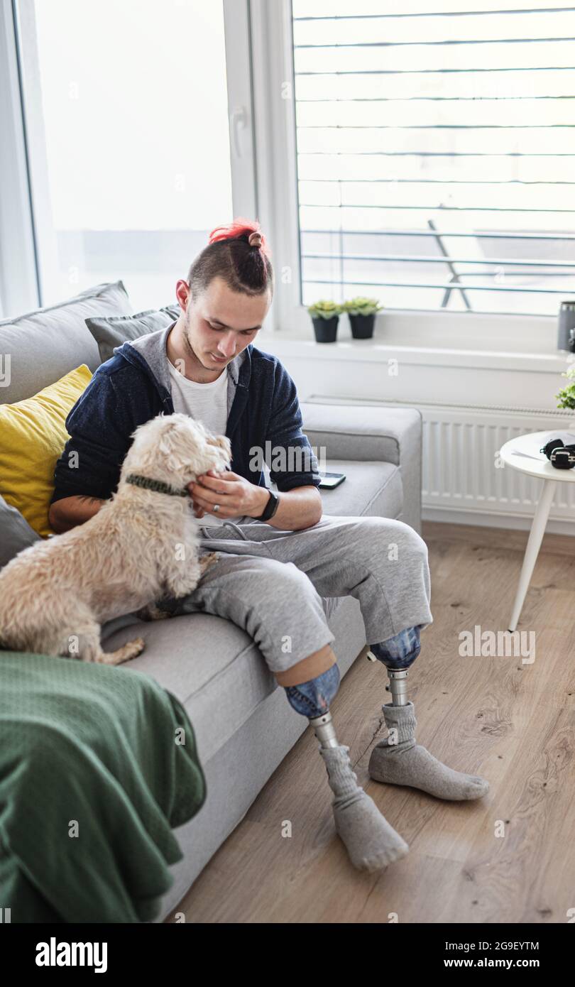 Portrait d'un jeune homme handicapé jouant avec un chien à l'intérieur à la maison, concept prothétique de jambe. Banque D'Images