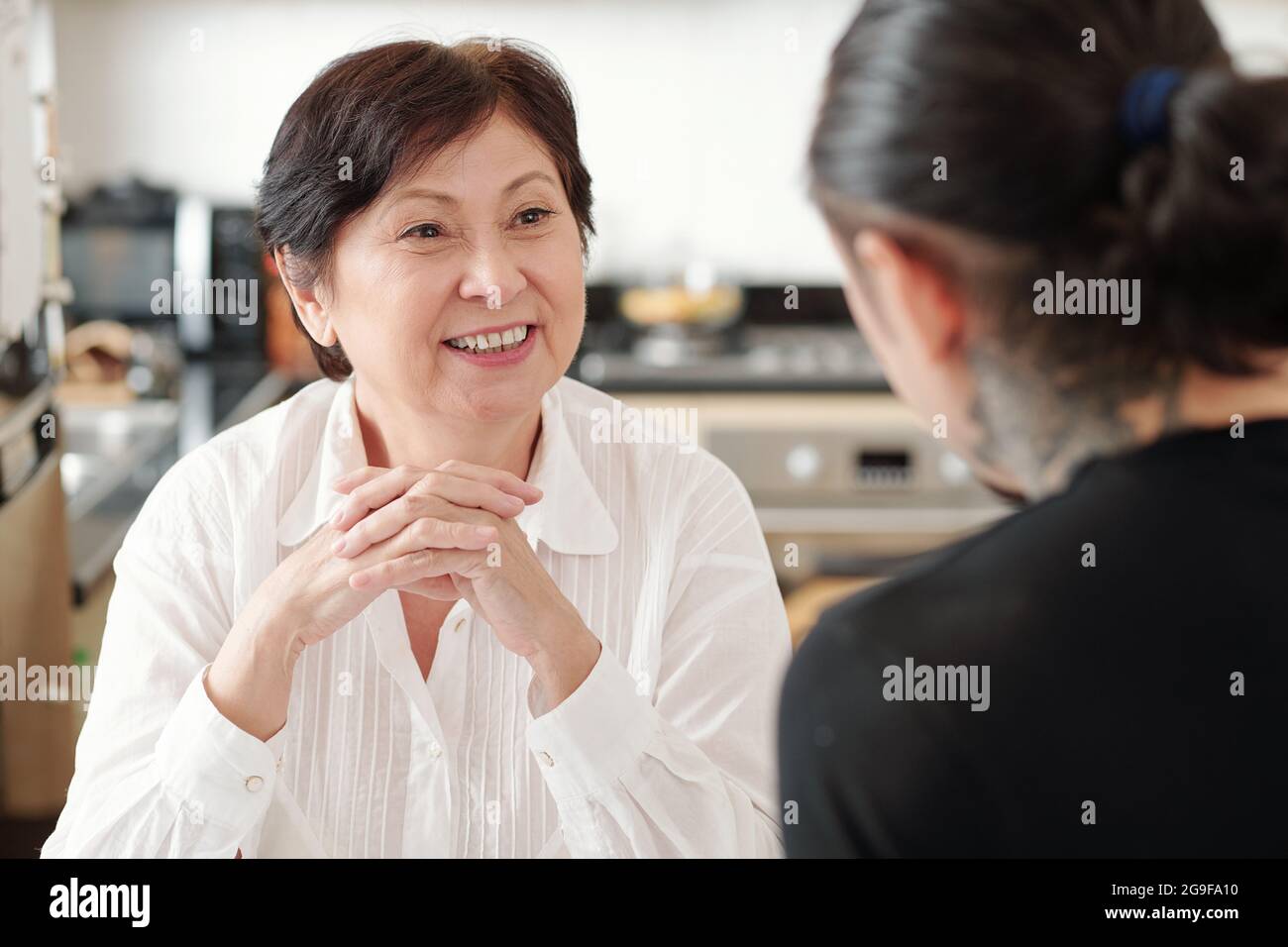 Femme asiatique mûre souriant et appréciant la conversation avec son fils aîné à la maison Banque D'Images