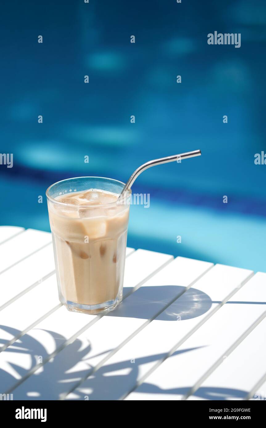 Café glacé Chypre Frappe Fredo contre l'eau bleue claire de la piscine, sur table blanche, avec paille métallique. Arrière-plan minimaliste d'été, holoïde Banque D'Images