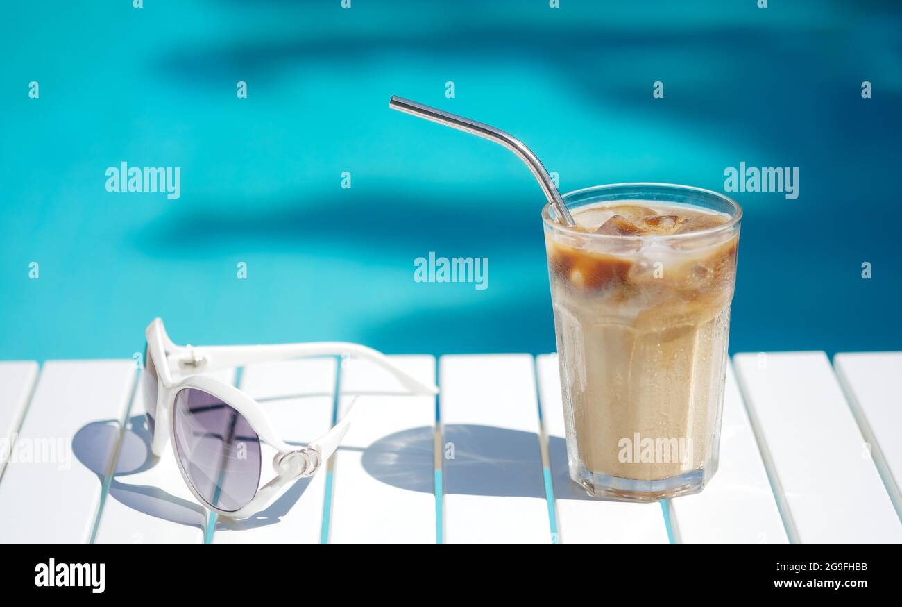 Café glacé Cyprus Frappe Fredo contre bleu eau claire de la piscine, sur table blanche, avec des lunettes de soleil. Arrière-plan minimaliste d'été, vacances Banque D'Images