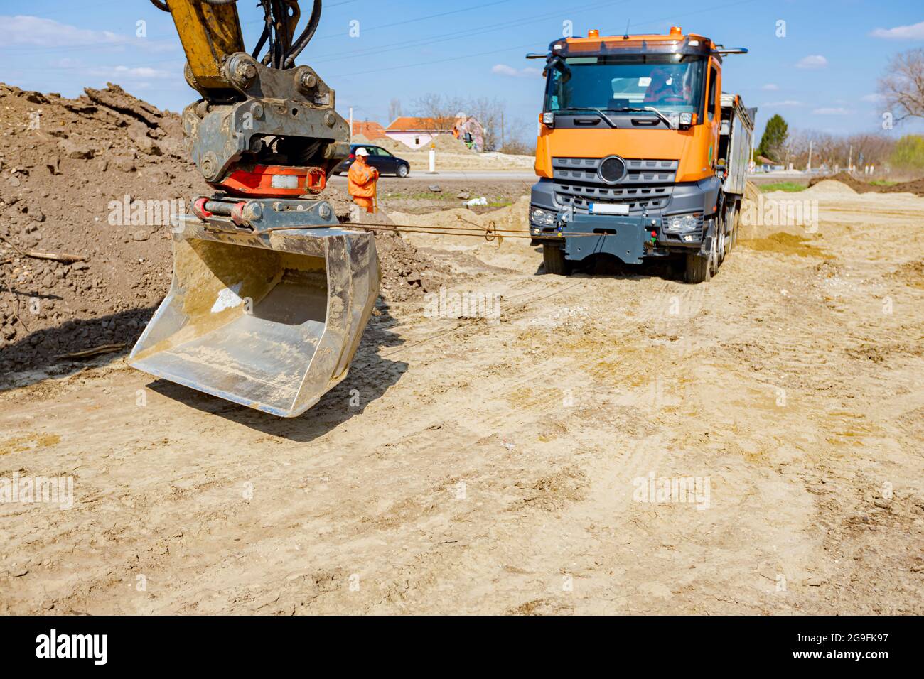 Une pelle tire un camion benne avec un cordon pour l'aider à sortir du sable sur le chantier. Banque D'Images