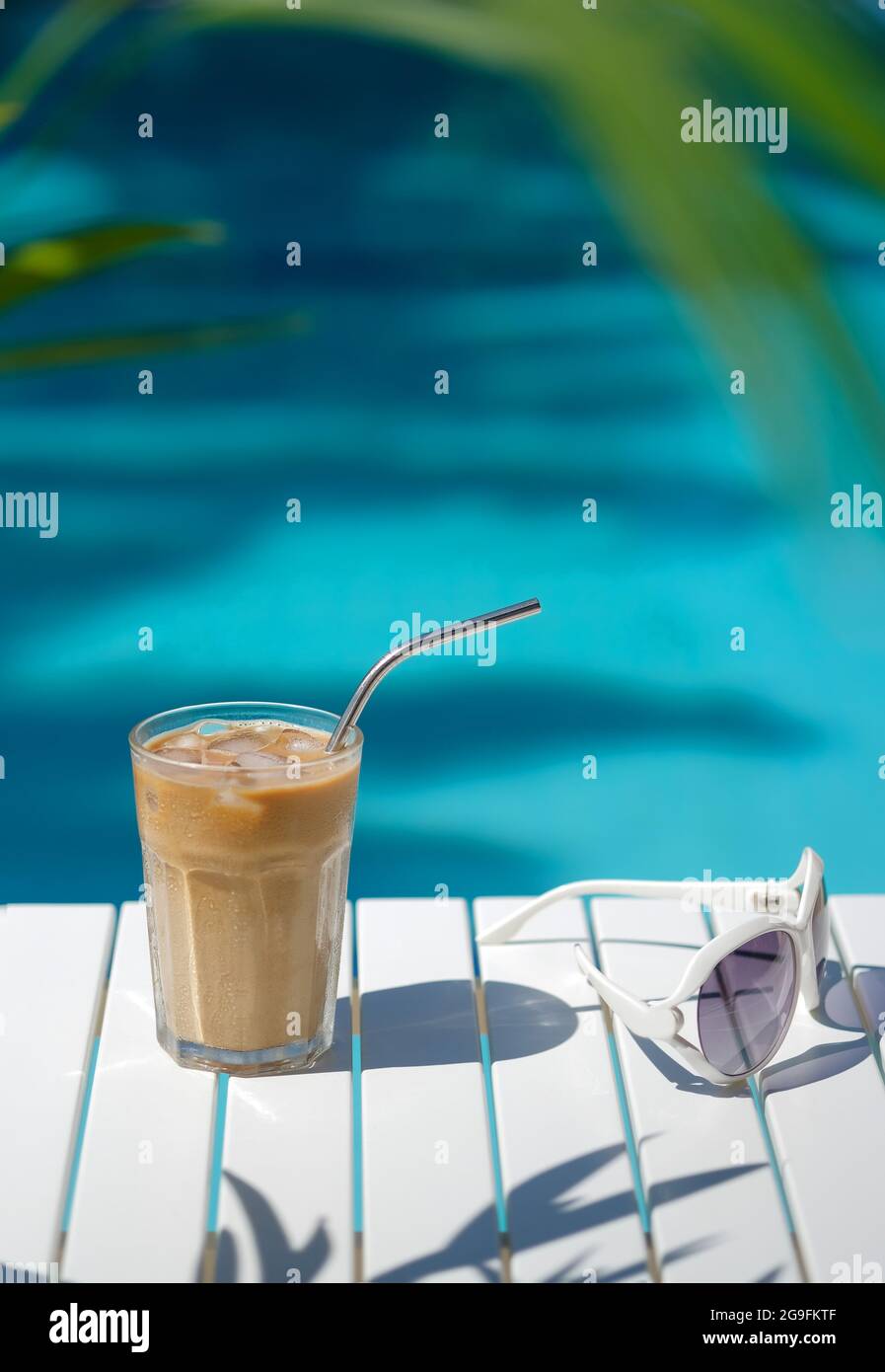 Café glacé Cyprus Frappe Fredo contre bleu eau claire de la piscine, sur table blanche, avec des lunettes de soleil. Arrière-plan minimaliste d'été, vacances Banque D'Images
