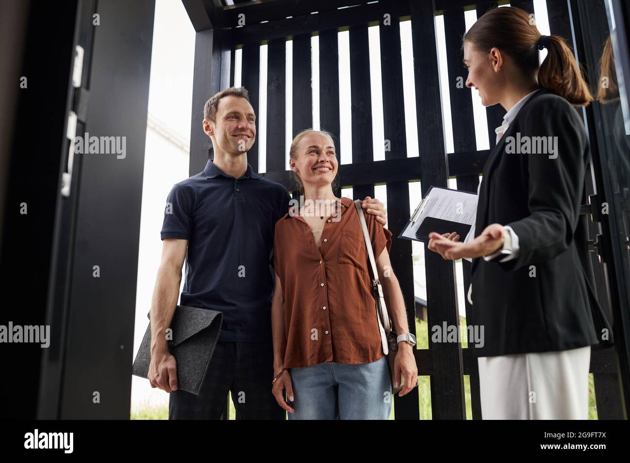 Portrait à faible angle d'une femme agent immobilier rencontrant un jeune couple debout dans la porte tout en achetant une nouvelle maison, un espace de copie Banque D'Images