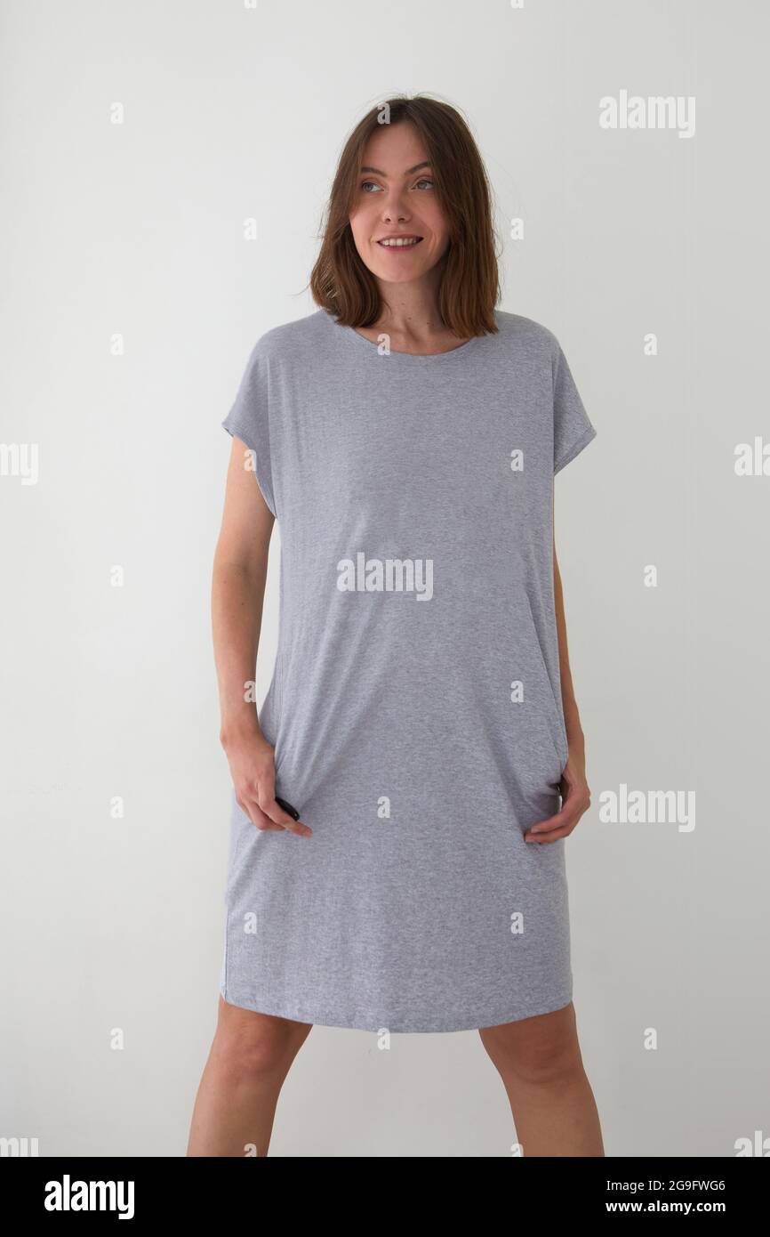 Positive femme porte des vêtements de nuit longs en coton debout avec les mains dans les poches sur fond blanc et regardant loin Banque D'Images