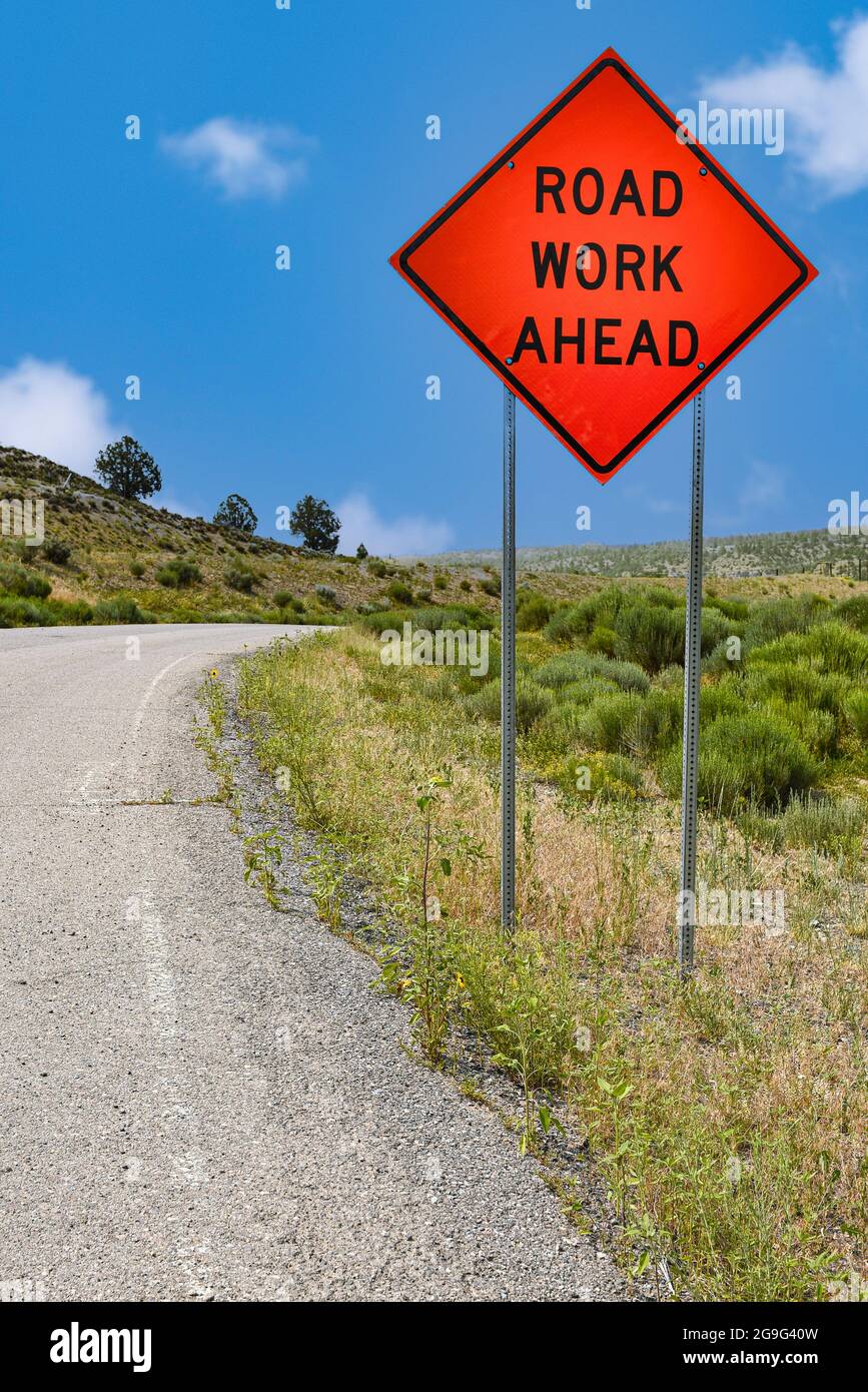 Un panneau en forme de losange orange vif le long d'une autoroute à deux voies au Nouveau-Mexique avertit les conducteurs de travaux routiers à venir. Banque D'Images
