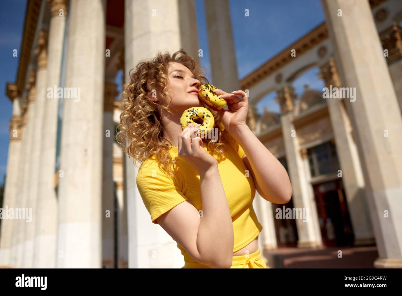Beauté mode modèle fille prenant des bonbons et des beignets colorés. Drôle joyeuse femme élégante avec des bonbons en ville. Concept de régime. Mauvaise alimentation, perte de poids Banque D'Images