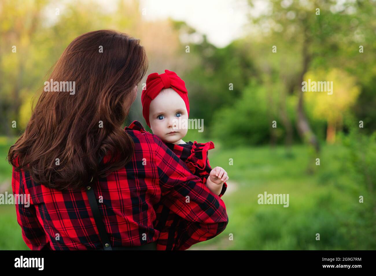 Portrait à yeux bleus adorable petite fille dans les bras de sa mère tout  en marchant. Maman embrassant avec sa fille à l'extérieur en été. Style  familial. Concept de maternité ou de