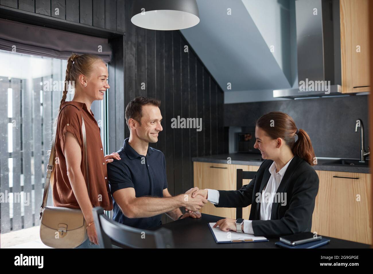 Vue latérale portrait d'un jeune couple qui se serre la main avec un agent immobilier tout en achetant une nouvelle maison, un espace de copie Banque D'Images