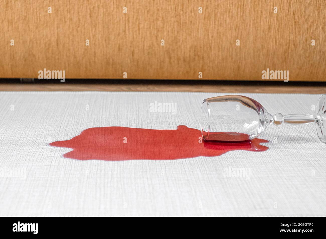 Du vin rouge s'est répandu près du canapé, sur un tapis blanc. Photo de haute qualité Banque D'Images