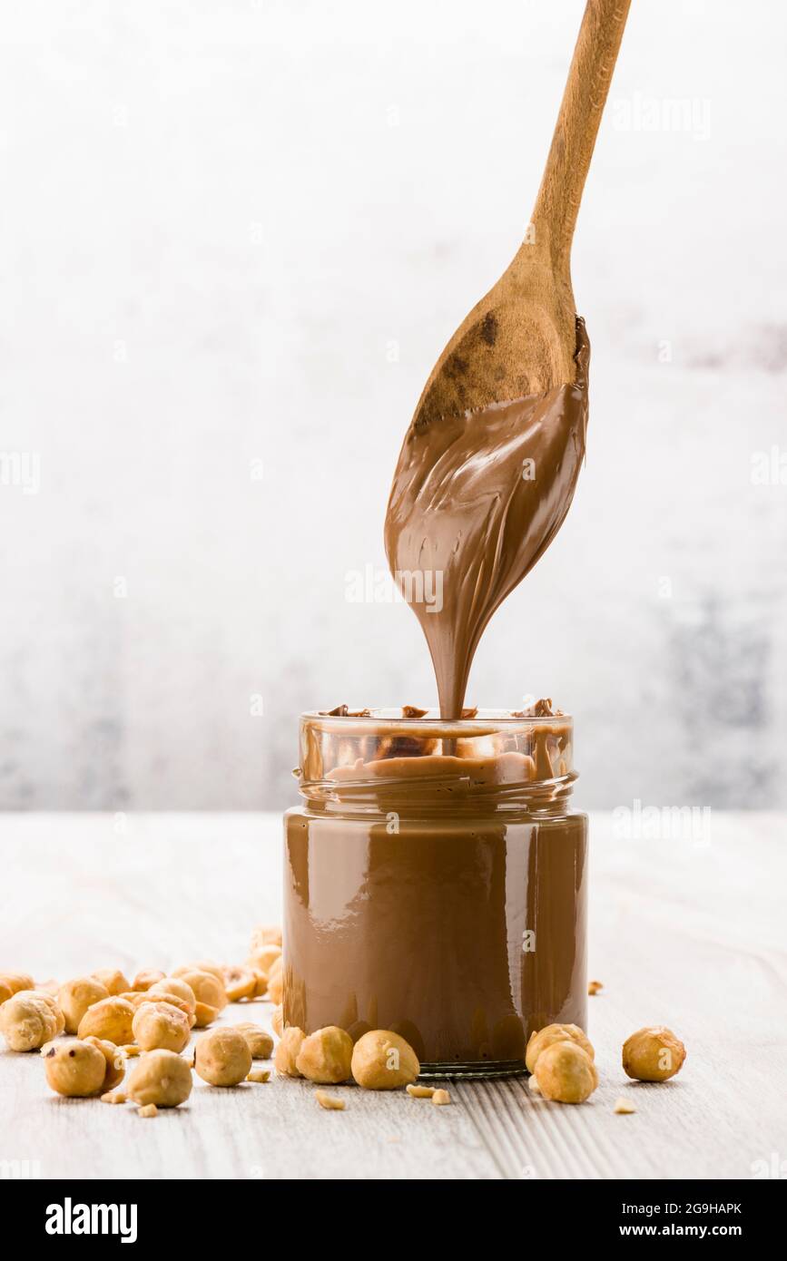 Crème au chocolat dans un pot en verre avec noisettes et cuillère à égoutter, sur une table en bois Banque D'Images
