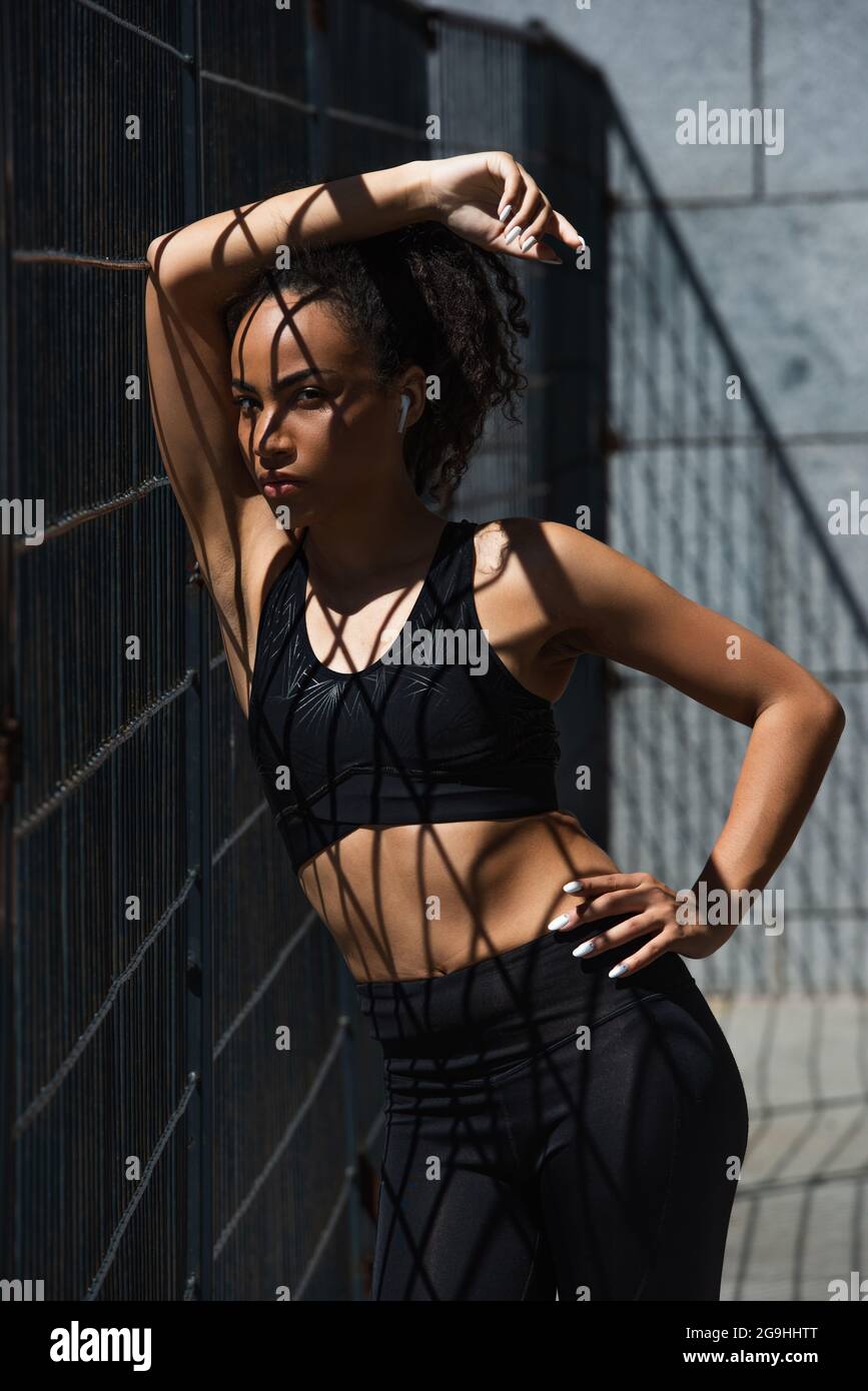 African american sportswoman en écouteur tenant la main sur la hanche près de la clôture Banque D'Images