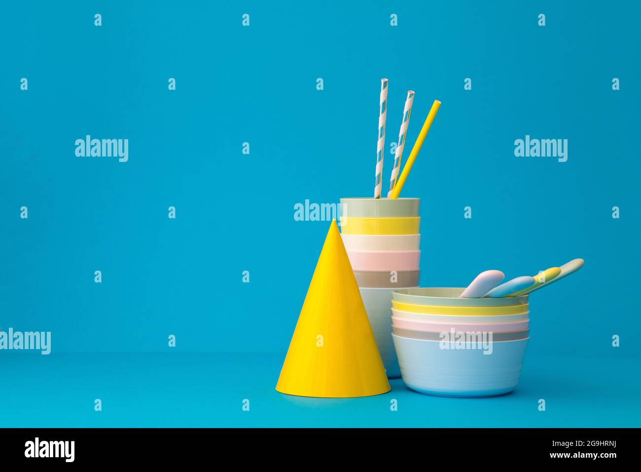 Composition avec vaisselle réutilisable en plastique multicolore avec pailles et chapeau de fête jaune brillant sur fond bleu Banque D'Images