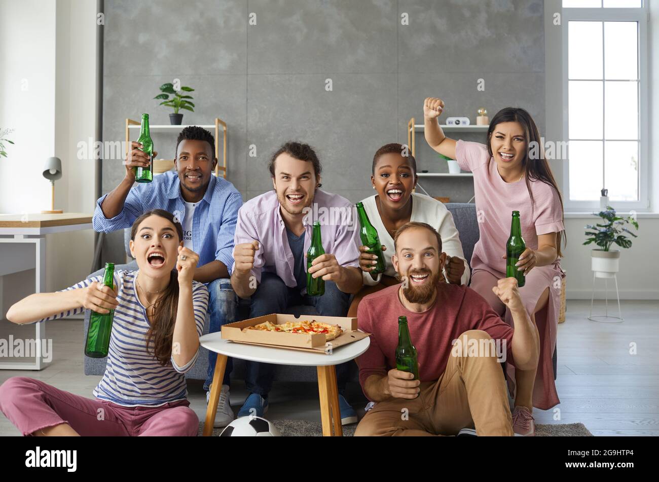 Groupe d'amis multiraciaux émotionnels et actifs regardant un match de football à la télévision à la maison. Banque D'Images