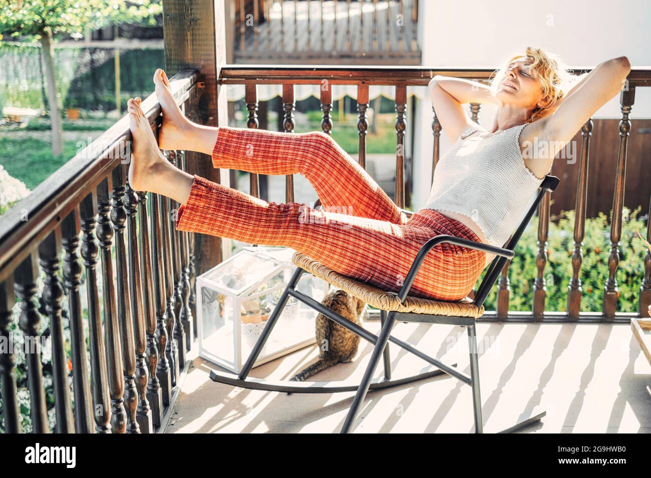 portrait d'une jeune femme blonde caucasienne mûre se détendant à la maison sur le porche assis dans une chaise à bascule. Concept de style de vie. Banque D'Images