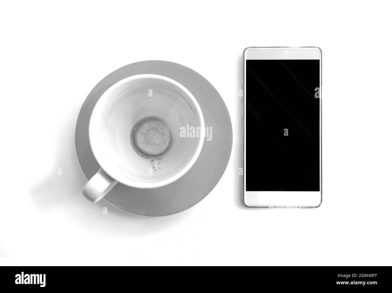 Videz la tasse de café fini avec le smartphone sur fond blanc en monochrome Banque D'Images