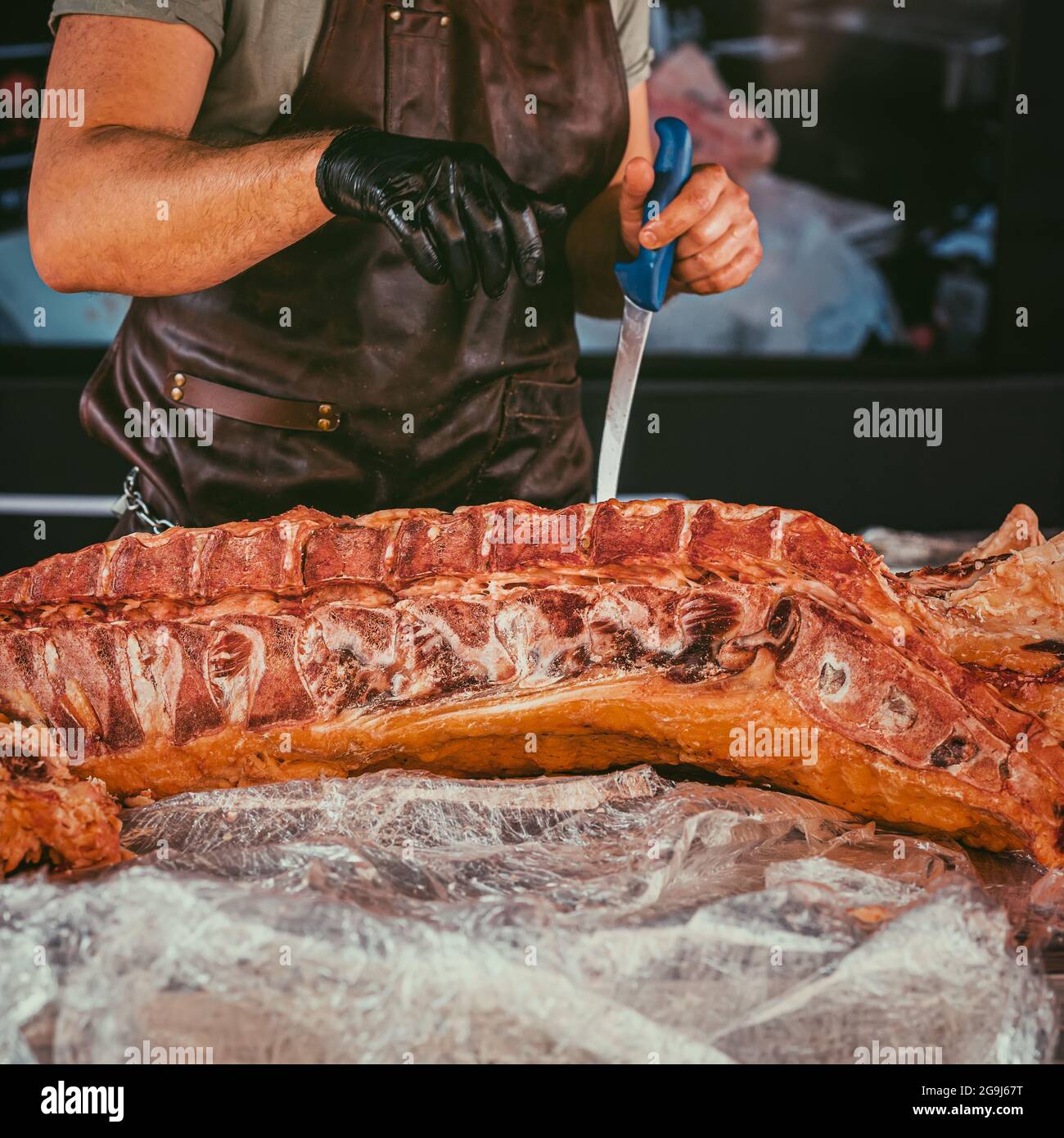 Boucher professionnel abstrait en tablier et gant en caoutchouc noir  coupant un énorme morceau de viande de bœuf cru sur le marché de la viande,  boucherie. Mise au point sélective Photo Stock -