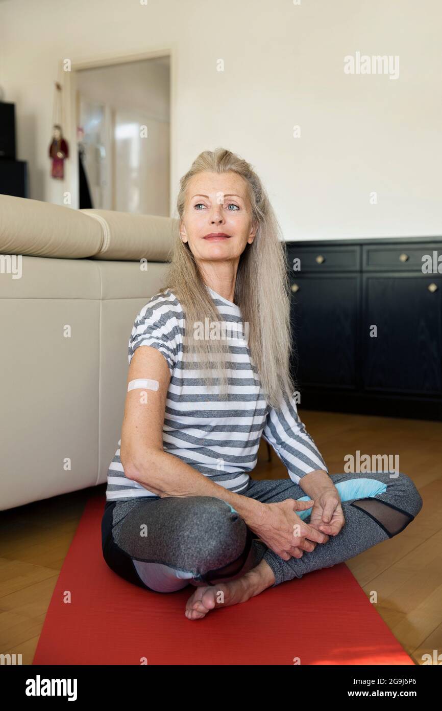 Autriche, Vienne, femme sénior avec bande adhésive sur le bras assis sur un tapis de yoga Banque D'Images