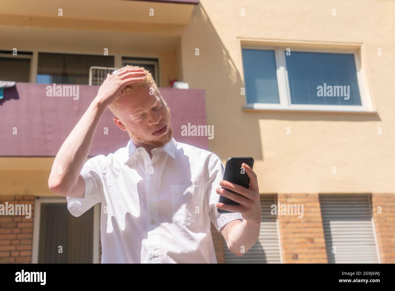 Allemagne, Cologne, Albino homme en chemise blanche tenant un smartphone Banque D'Images