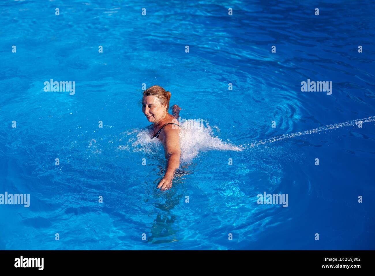 Une belle femme caucasienne profite d'un massage hydro dos et cou avec un jet d'eau dans une piscine extérieure en vacances Banque D'Images