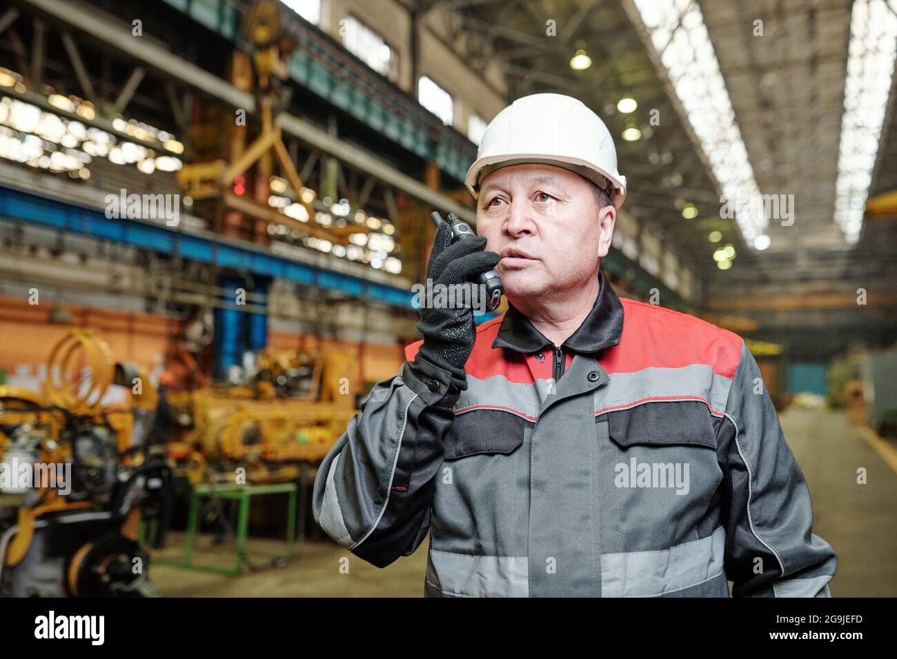 Ingénieur sérieux et mature dans la tenue de casque de documents travaillant en production usine Banque D'Images