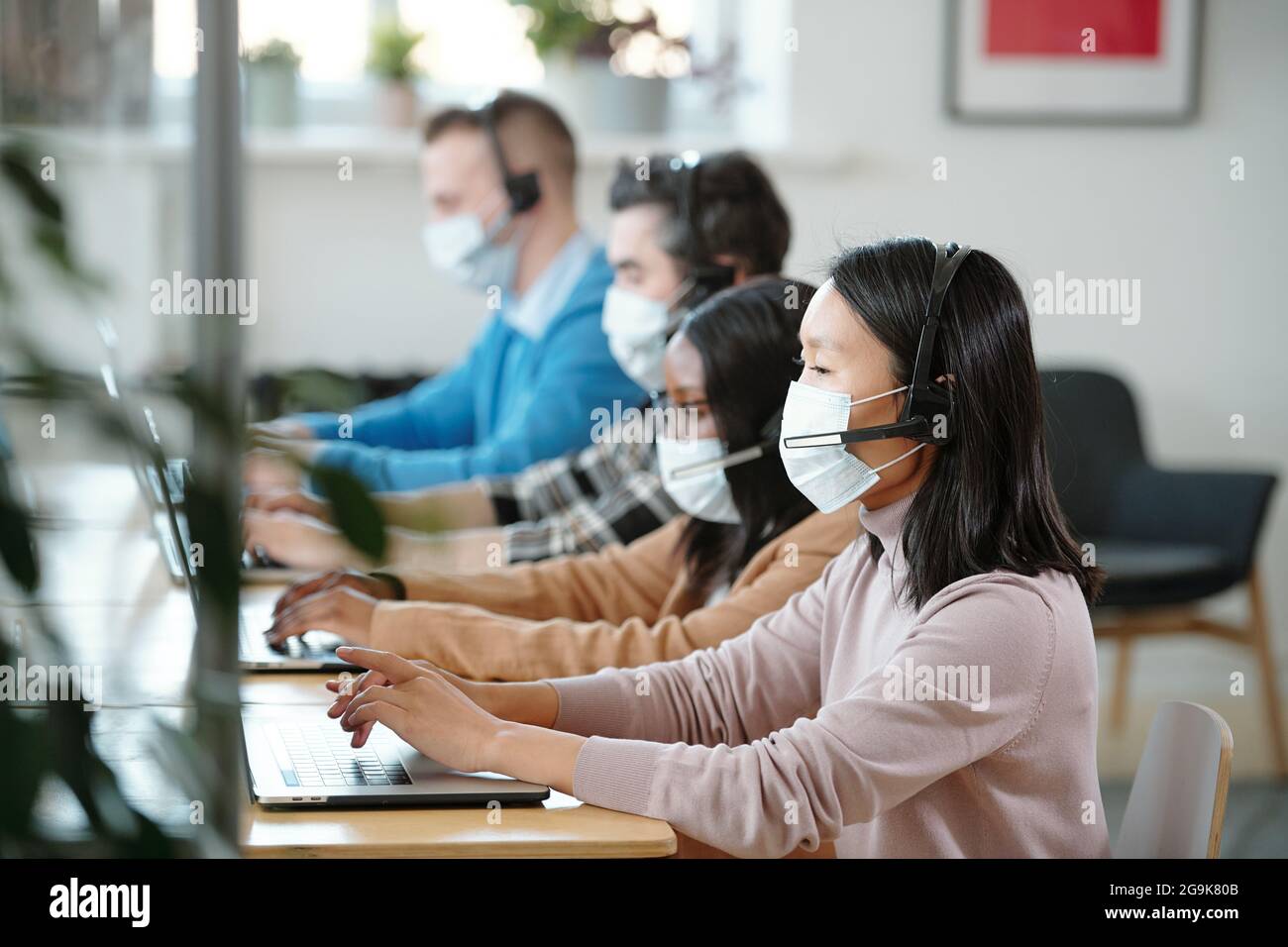 Plusieurs jeunes opréateurs interculturels avec des ordinateurs portables consultant des clients en ligne au bureau Banque D'Images