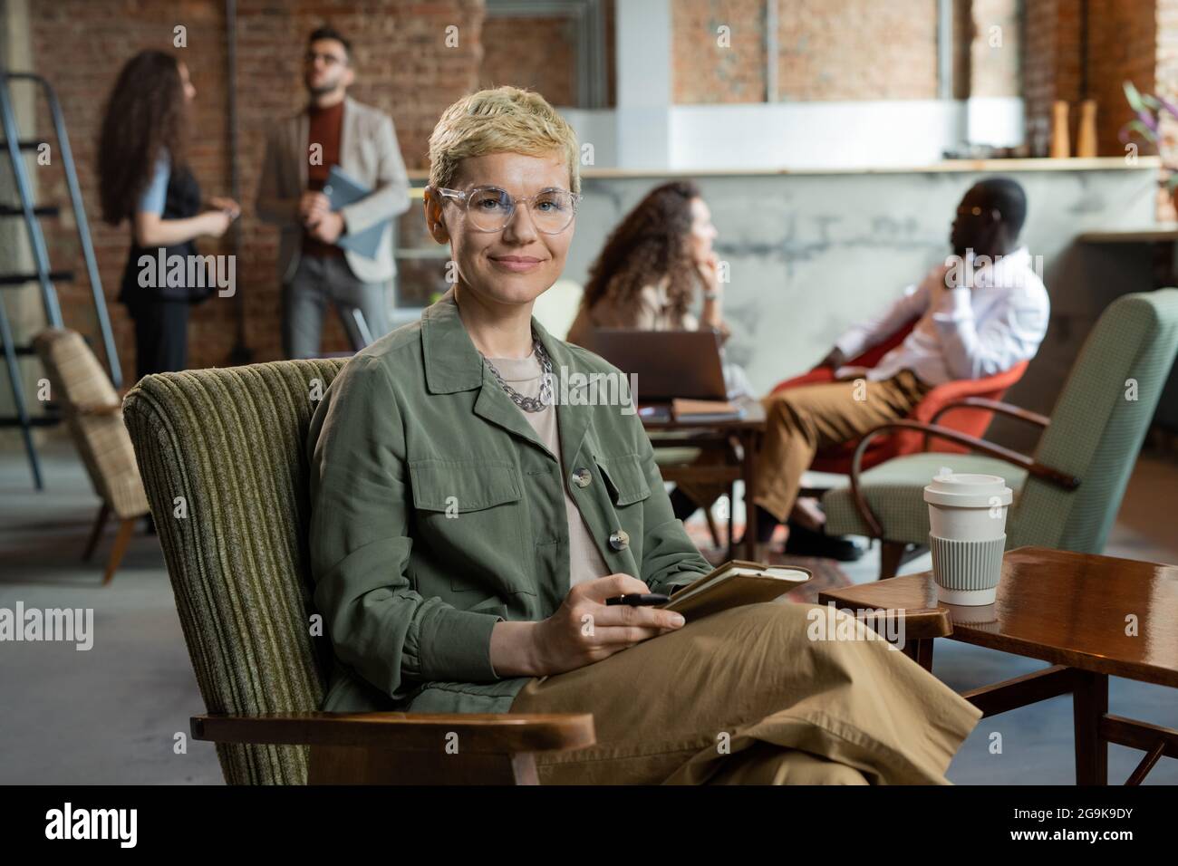 Jeune femme d'affaires souriante aux cheveux blonds courts, assise dans un fauteuil Banque D'Images