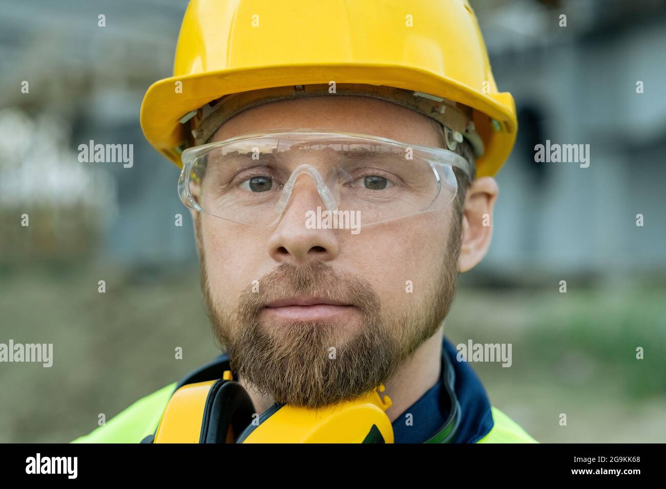 Gros plan de l'ouvrier de construction dans un casque de travail et dans des lunettes de protection regardant la caméra Banque D'Images