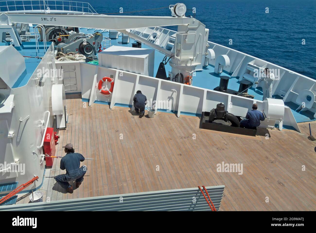 En regardant vers le bas sur l'équipage de marins de la marine marchande travaillant sur l'arc exposé peinture des surfaces en acier contre la rouille navire de croisière pont de paquebot à la mer en Méditerranée Banque D'Images