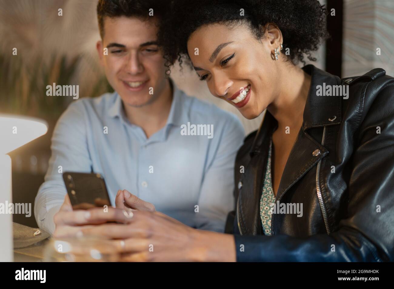Couple multiracial souriant de jeunes utilisant un smartphone assis sur la table d'un restaurant. Personnes utilisant le concept de technologie. Banque D'Images