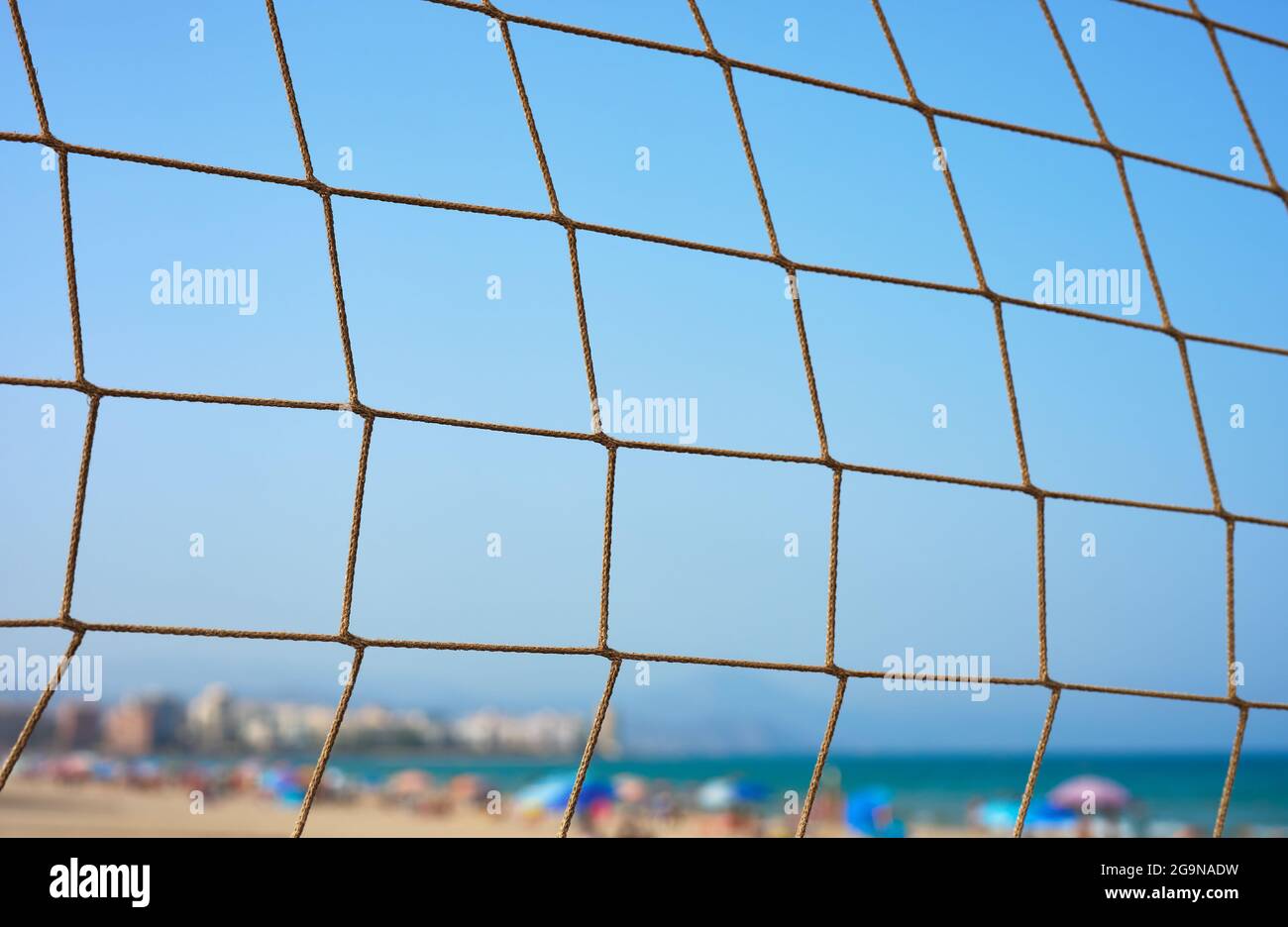 détail d'une plage avec des touristes et des bâtiments en arrière-plan à travers un filet de volley Banque D'Images