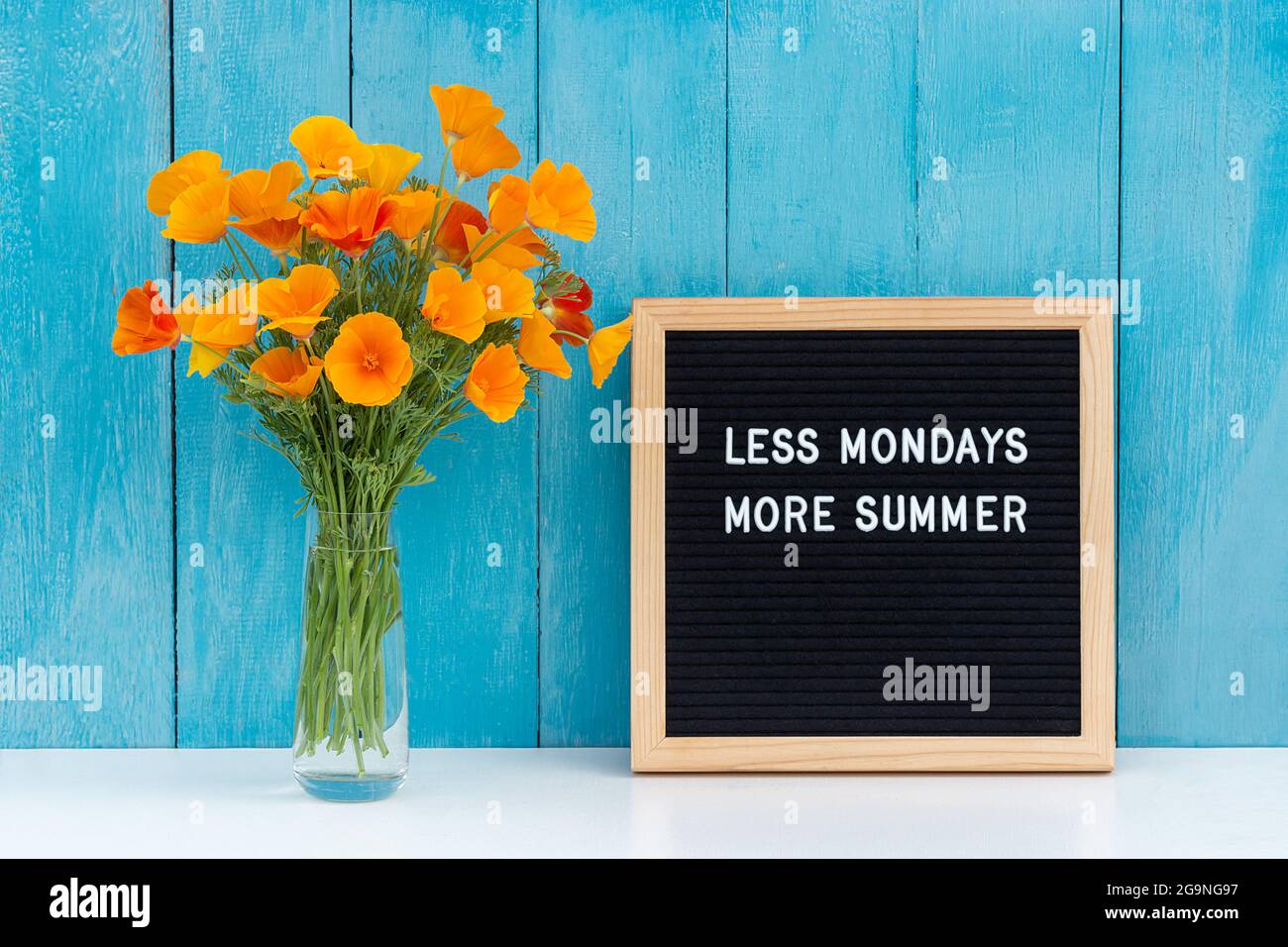 Moins De Lundis Plus D Ete Citation Motivationnelle Sur Le Panneau De Lettres Et Bouquet De Fleurs Orange Sur La Table Blanche Contre Le Mur En Bois Bleu Concept Inspire Photo Stock