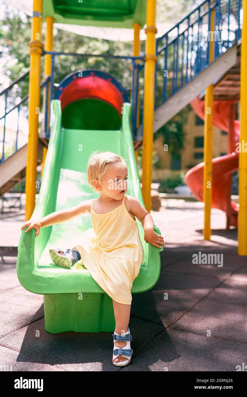 Une petite fille dans une robe monte sur le toboggan des enfants, en  tournant sa tête sur le côté Photo Stock - Alamy