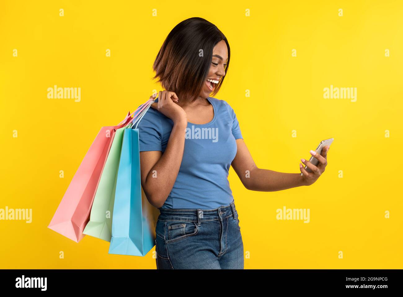 Femme africaine avec smartphone et sacs de shopping posant, fond jaune Banque D'Images