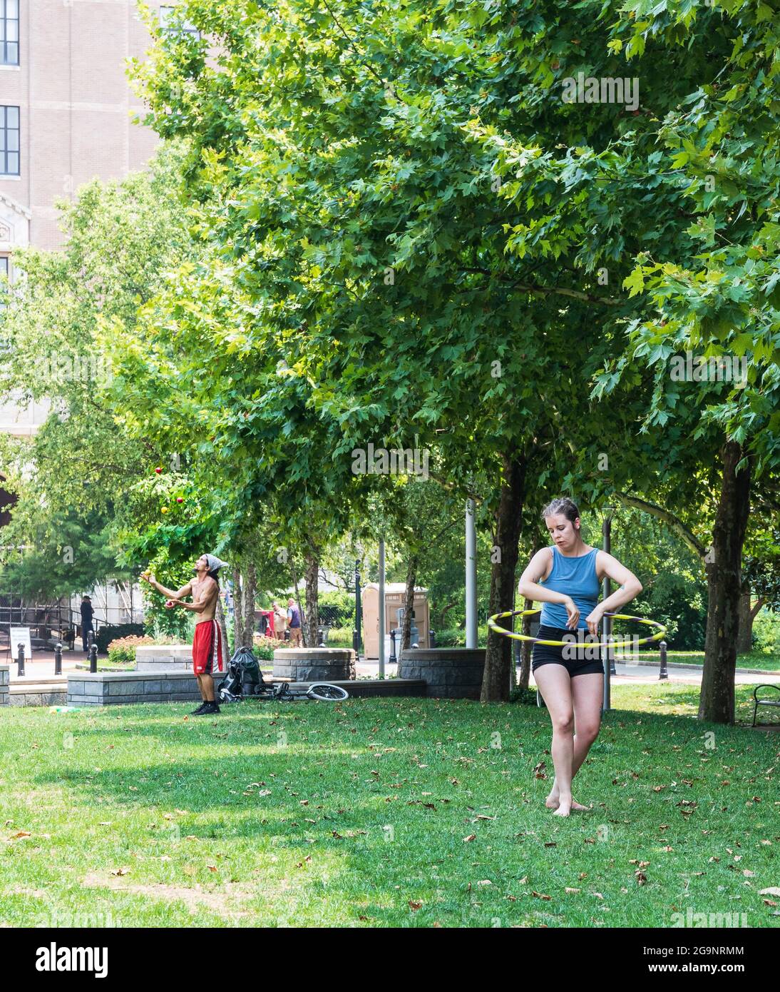 ASHEVILLE, NC, USA-22 JUILLET 2021: Un homme et une femme se produit à Pack Square, elle avec un hula hoop, il jongle balles. Végétation luxuriante en arrière-plan. Banque D'Images