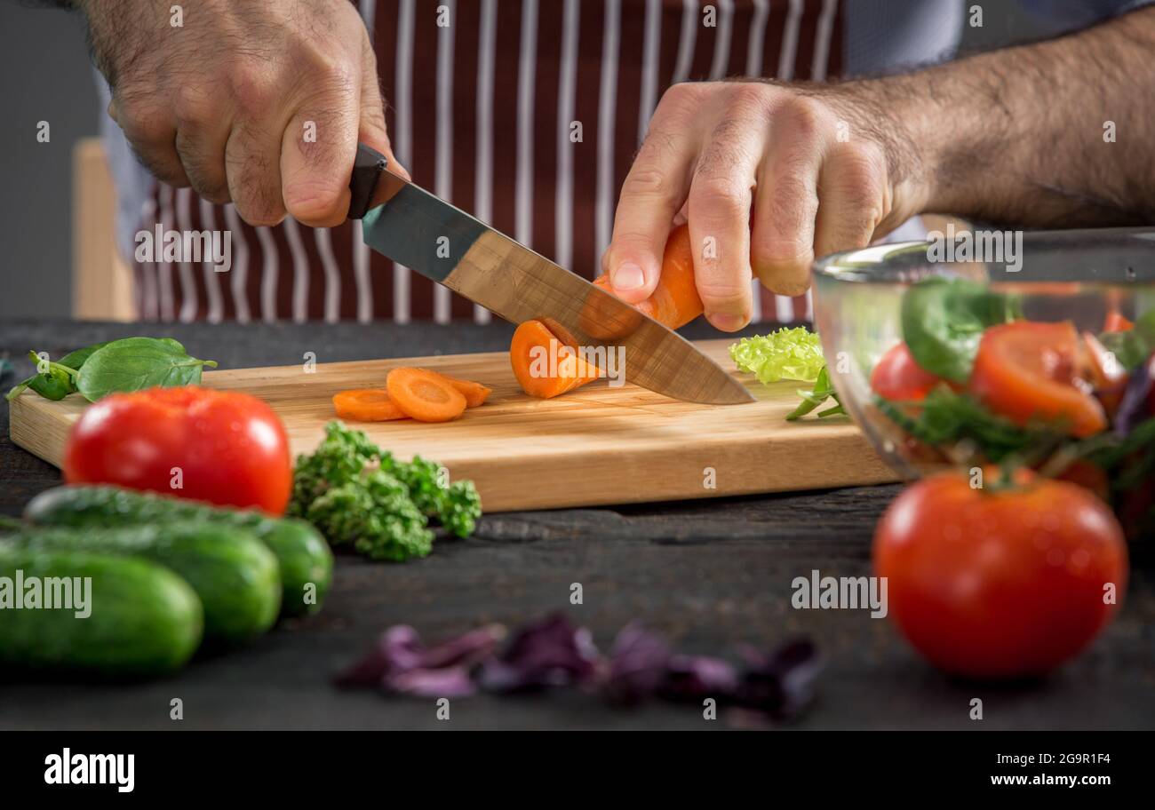 Close up on coupe les mains des hommes, faisant de carottes salade. Couper les légumes en chef. Mode de vie sain, alimentation nourriture Banque D'Images