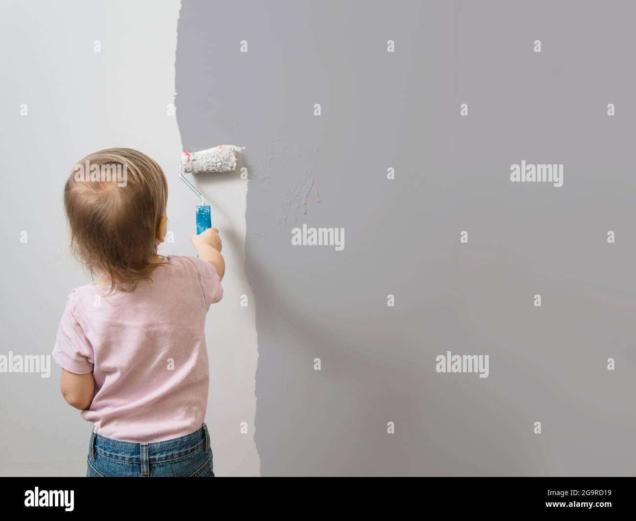 Un petit enfant peint le mur avec du rouleau et de la peinture grise, un fond vide. Décoration intérieure, reconception, espace de copie Banque D'Images