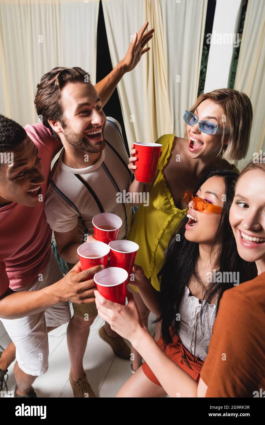 Des amis interraciaux souriants et excités se savourent avec un verre dans le patio pendant la fête Banque D'Images