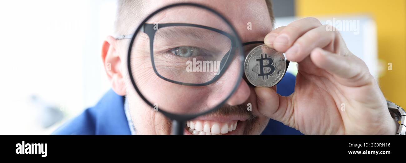 L'homme regarde à travers la loupe et tient le bitcoin dans son main Banque D'Images