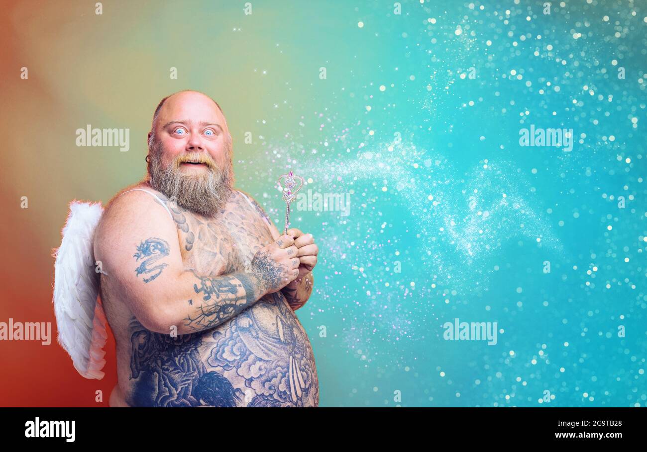 Gros homme émerveillé avec la barbe, tatouages et ailes agit comme une fée magique Banque D'Images