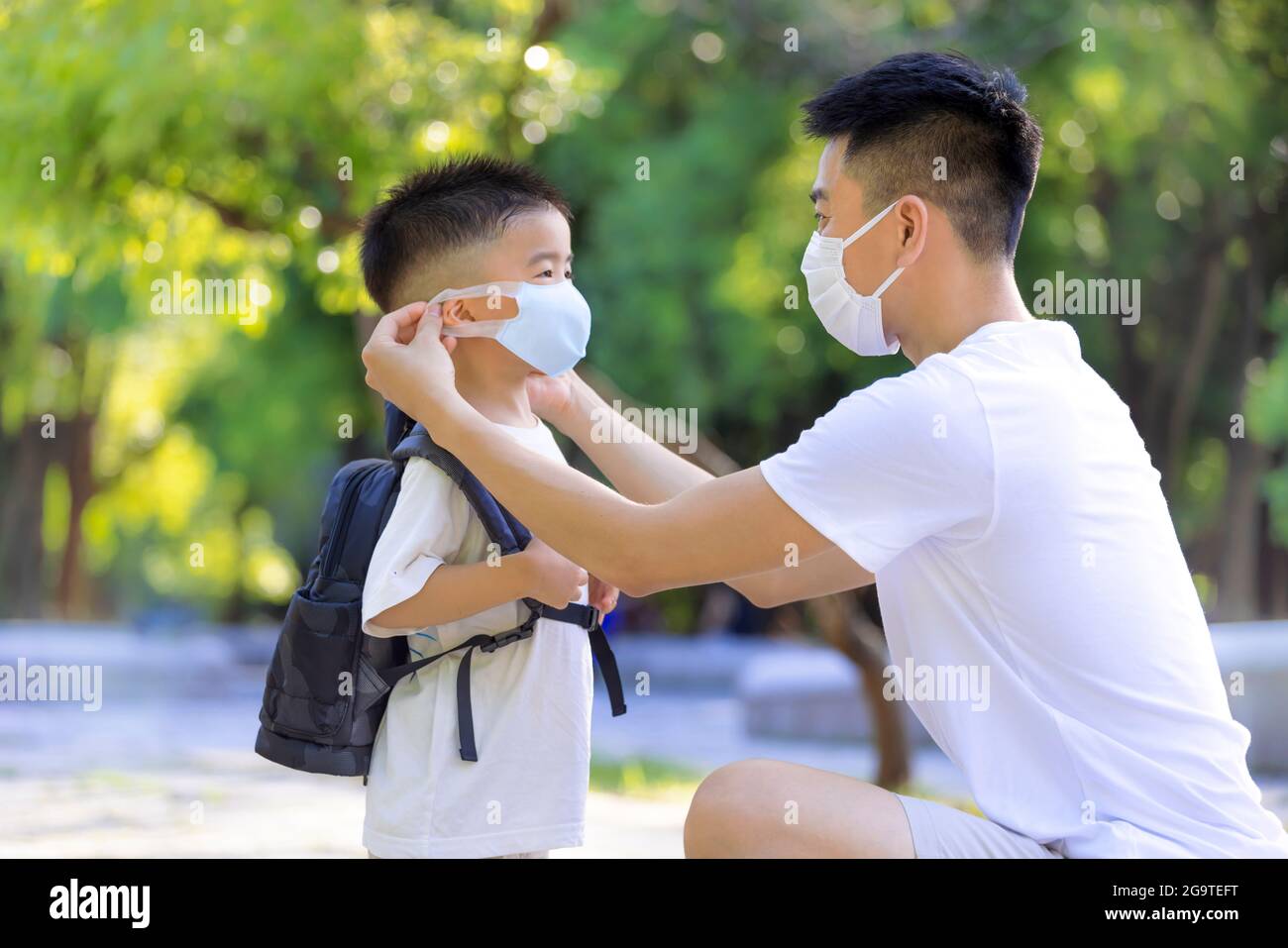 Le père aide son fils à porter un masque médical pour la protection Covid-19 Banque D'Images