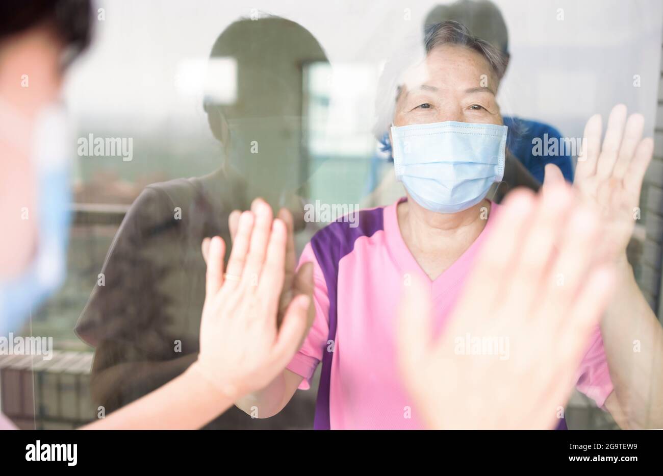 La femme âgée en masque médical communique avec sa fille par la fenêtre. Personnes âgées en quarantaine, isolées. Coronavirus pandémique covid-19 Banque D'Images